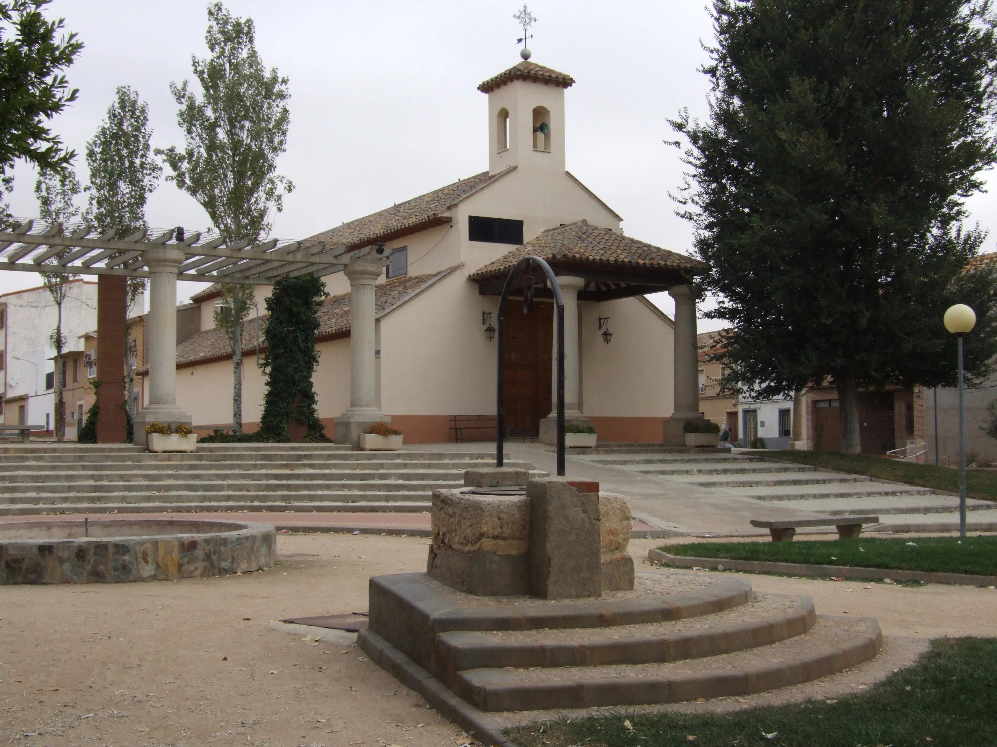 Capilla de fachada clara con pozo y escalinata en la plaza