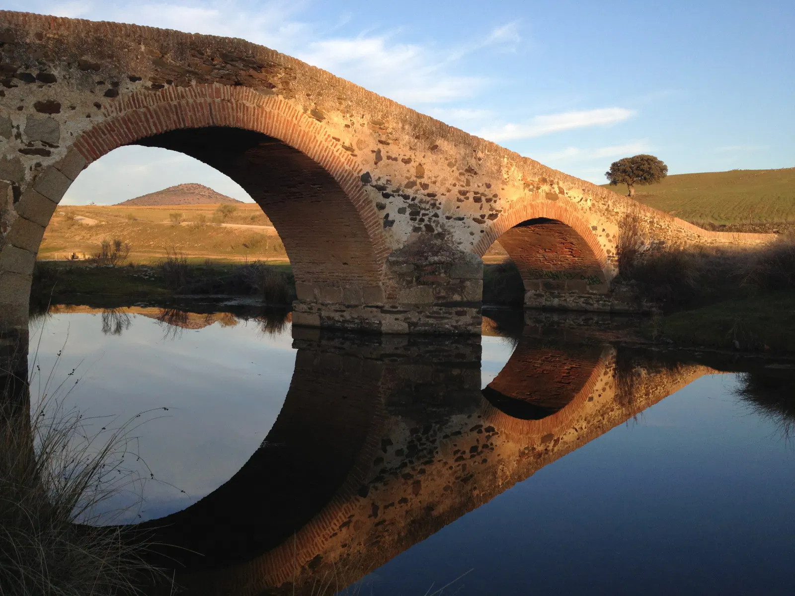 Puente de piedra de dos arcos reflejado en el agua